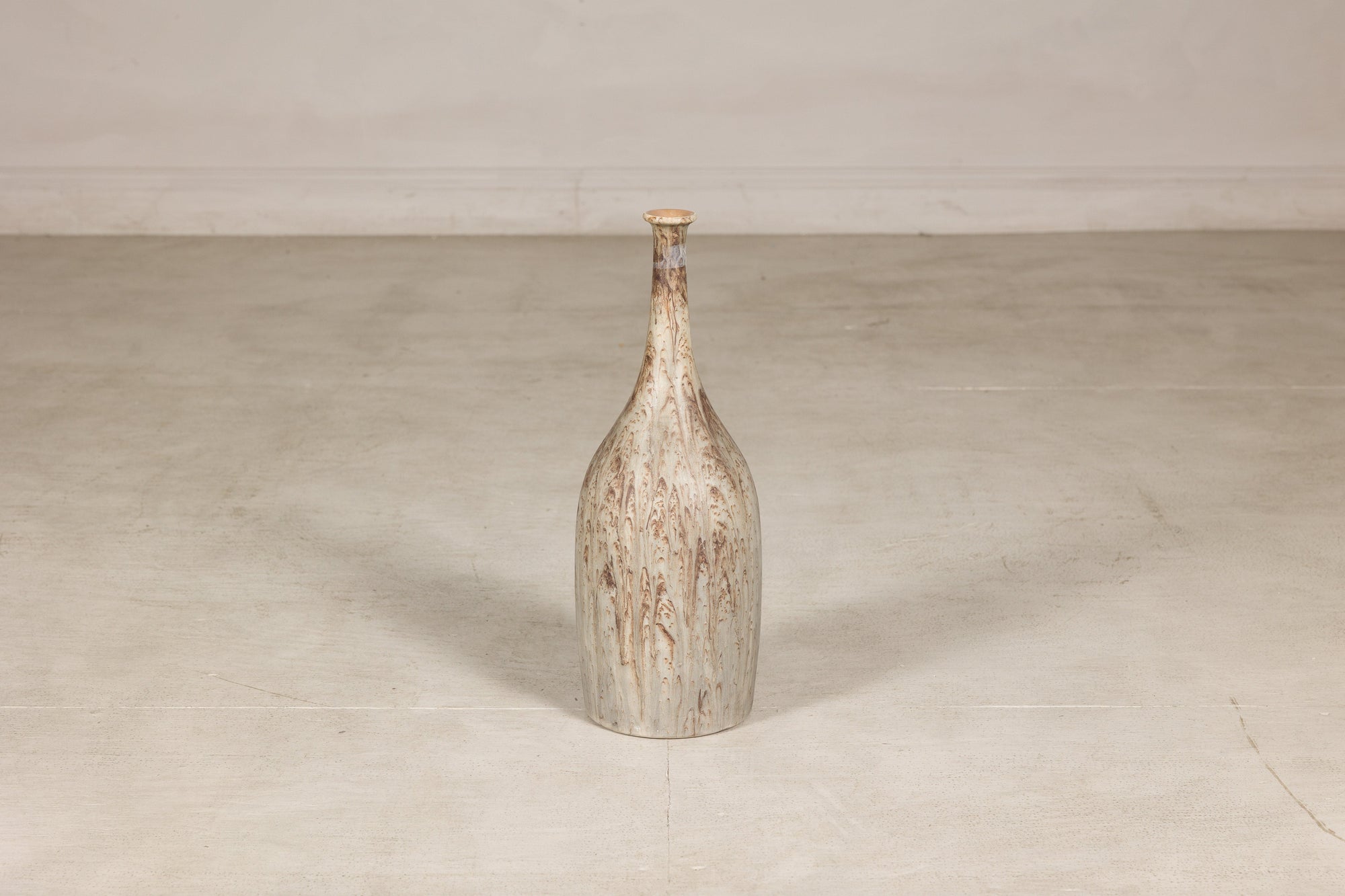 Cream and brown drip-glazed ceramic bottle vase on a light floor against a pale wall.
