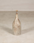 Cream and brown drip-glazed ceramic bottle vase on a light floor against a pale wall.