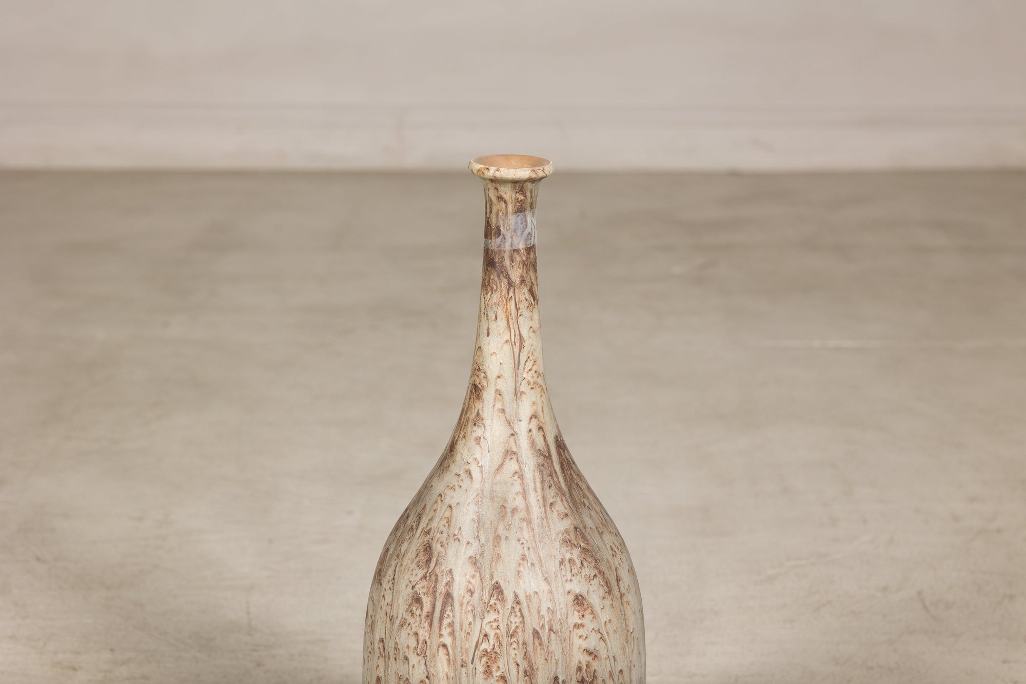 Cream and brown drip-glazed ceramic bottle vase with narrow neck, close-up against a light background.