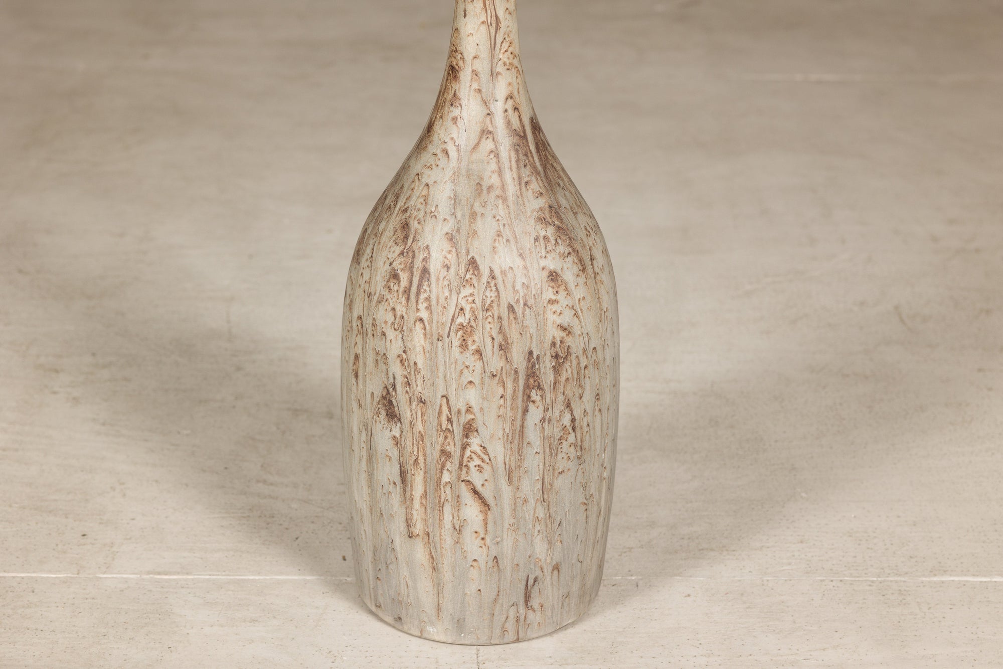 Close-up of tall cream and brown drip-glazed ceramic bottle vase with narrow neck and textured hand-finished surface.