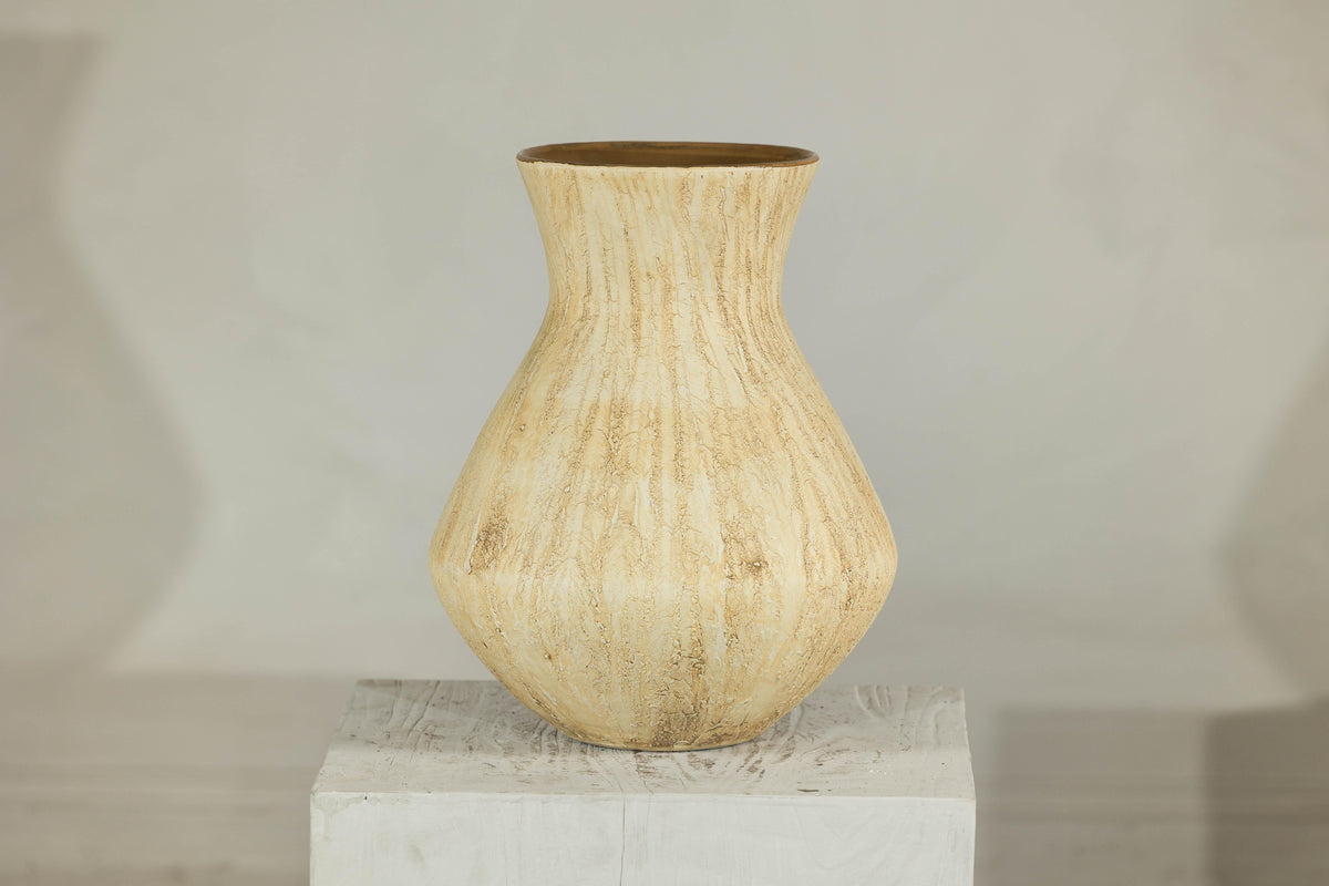 Beige textured ceramic vase with drip glaze and flared neck on white wooden pedestal.