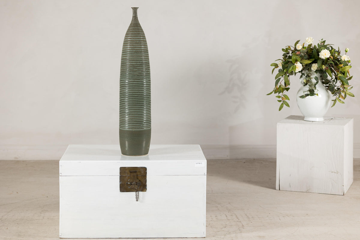 Green-glazed ceramic vase with a ribbed body on a white wooden chest.