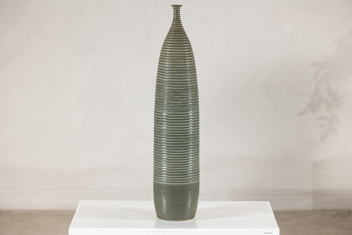 Green-glazed ribbed ceramic vase on white surface.