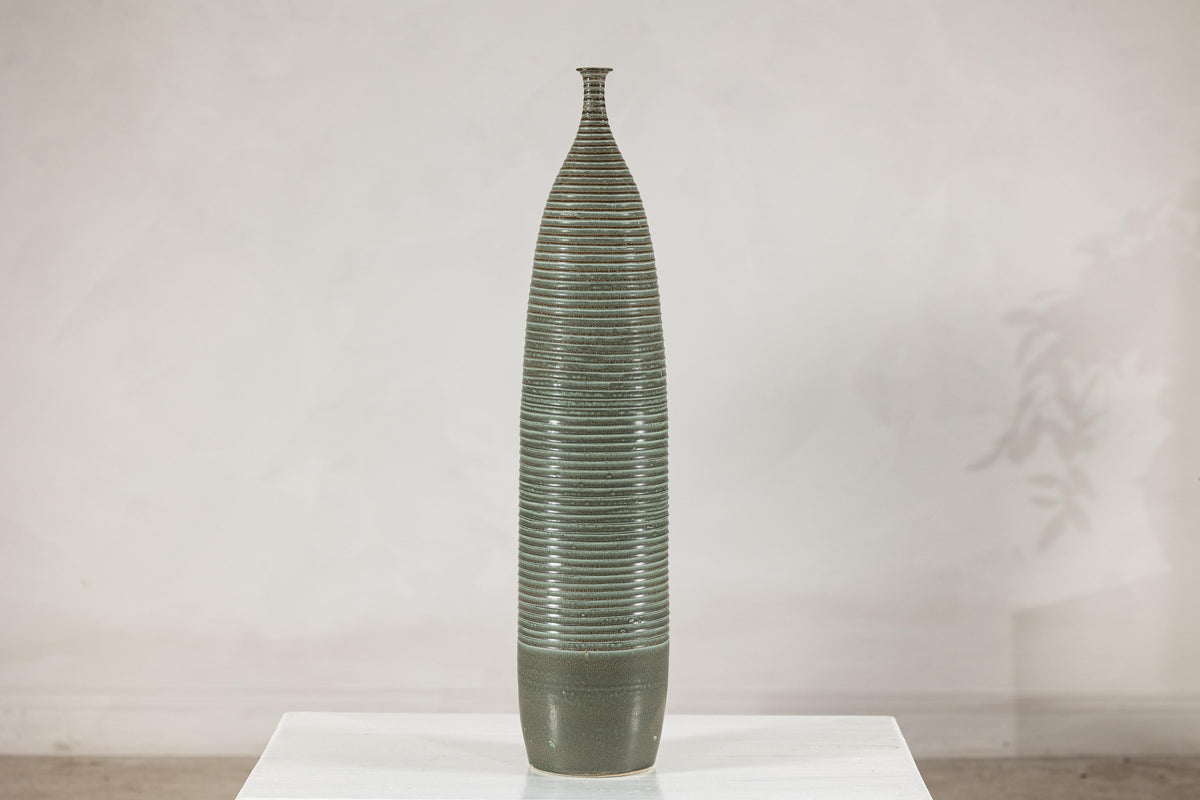 Green-glazed ribbed ceramic vase on a white table.