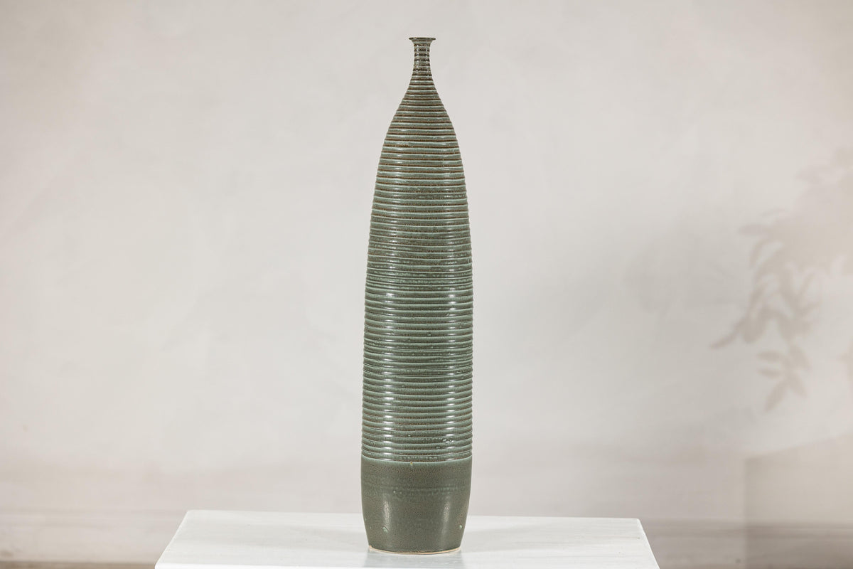 Tall green-glazed ribbed ceramic vase on a white table.
