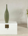 Olive-green ribbed ceramic artisan vase on a white wooden chest.