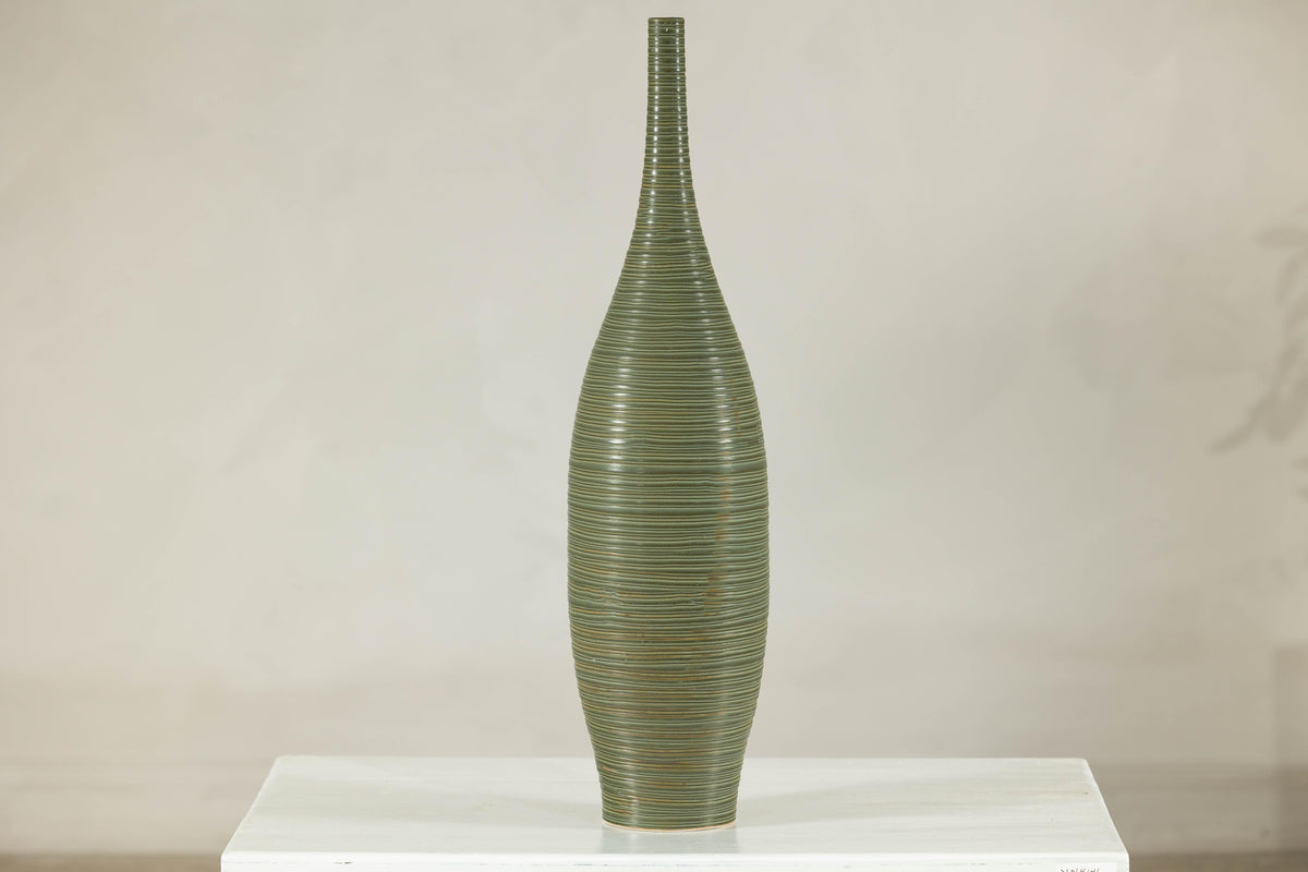 Olive-green ribbed ceramic artisan vase on white surface.