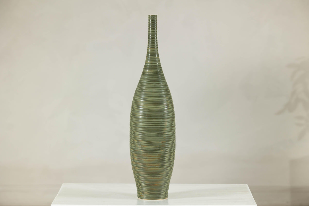 Olive-green ribbed ceramic artisan vase on white surface.