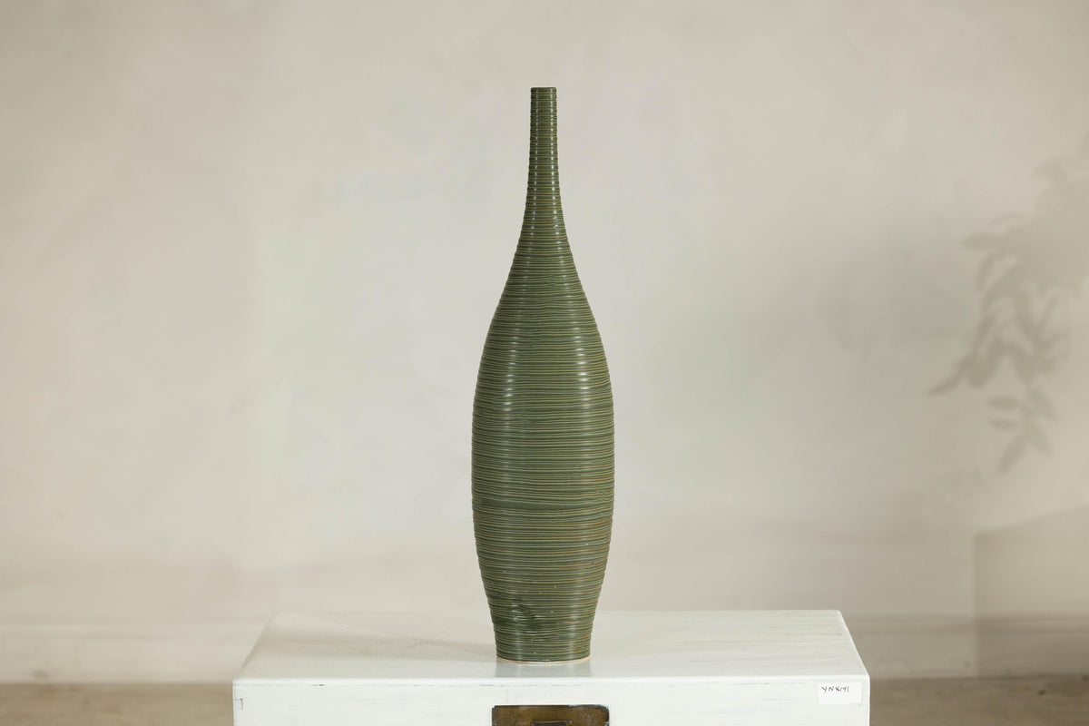 Olive-green ribbed ceramic artisan vase on white table.