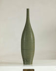 Olive-green ribbed ceramic artisan vase on white table.