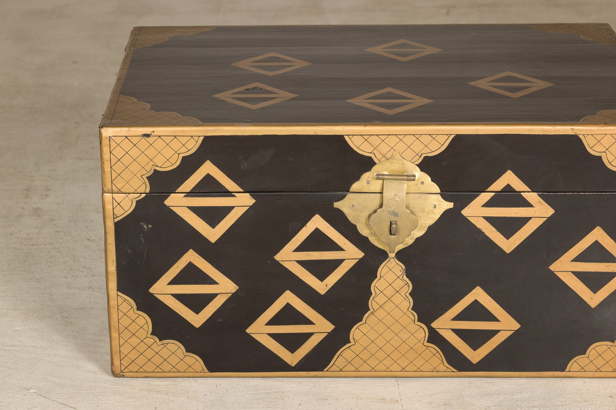 Black lacquered Chinese chest with gold geometric decoration and brass latch on a light-colored surface.