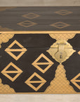 Black lacquered Chinese chest with gold geometric decoration and brass latch on a light-colored surface.