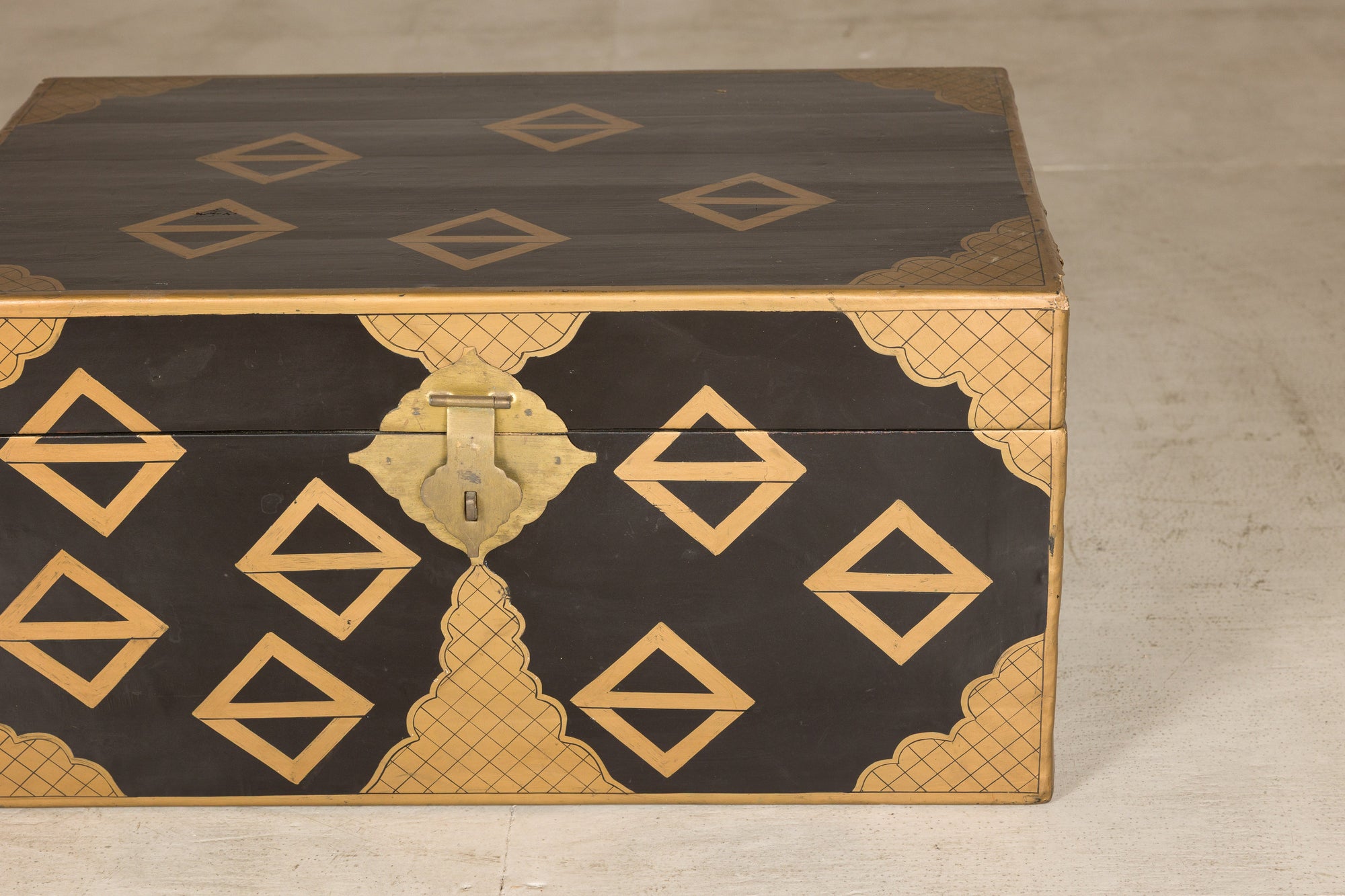 Black lacquered Chinese chest with gold geometric design and brass lock, displayed on a light-colored surface.