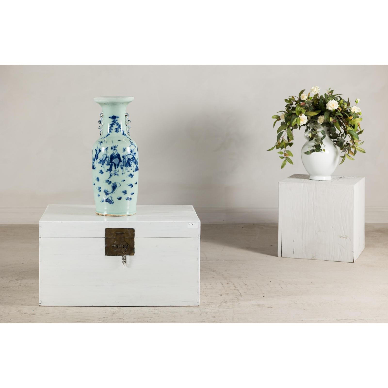 Close-up of an antique Chinese blue and white porcelain vase with scenes and celadon glaze beside a cobalt blue vase.