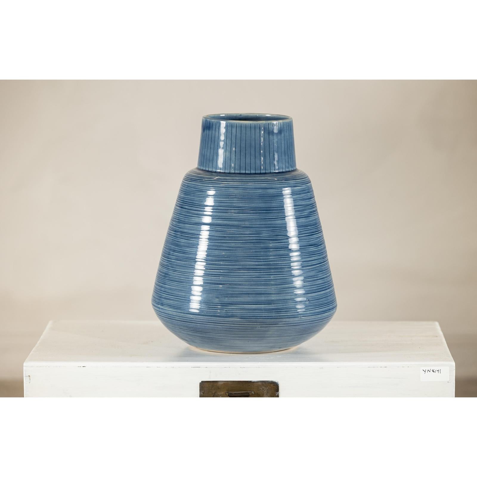 Blue-glazed ceramic vase with tapering form and horizontal ridges on a white surface.