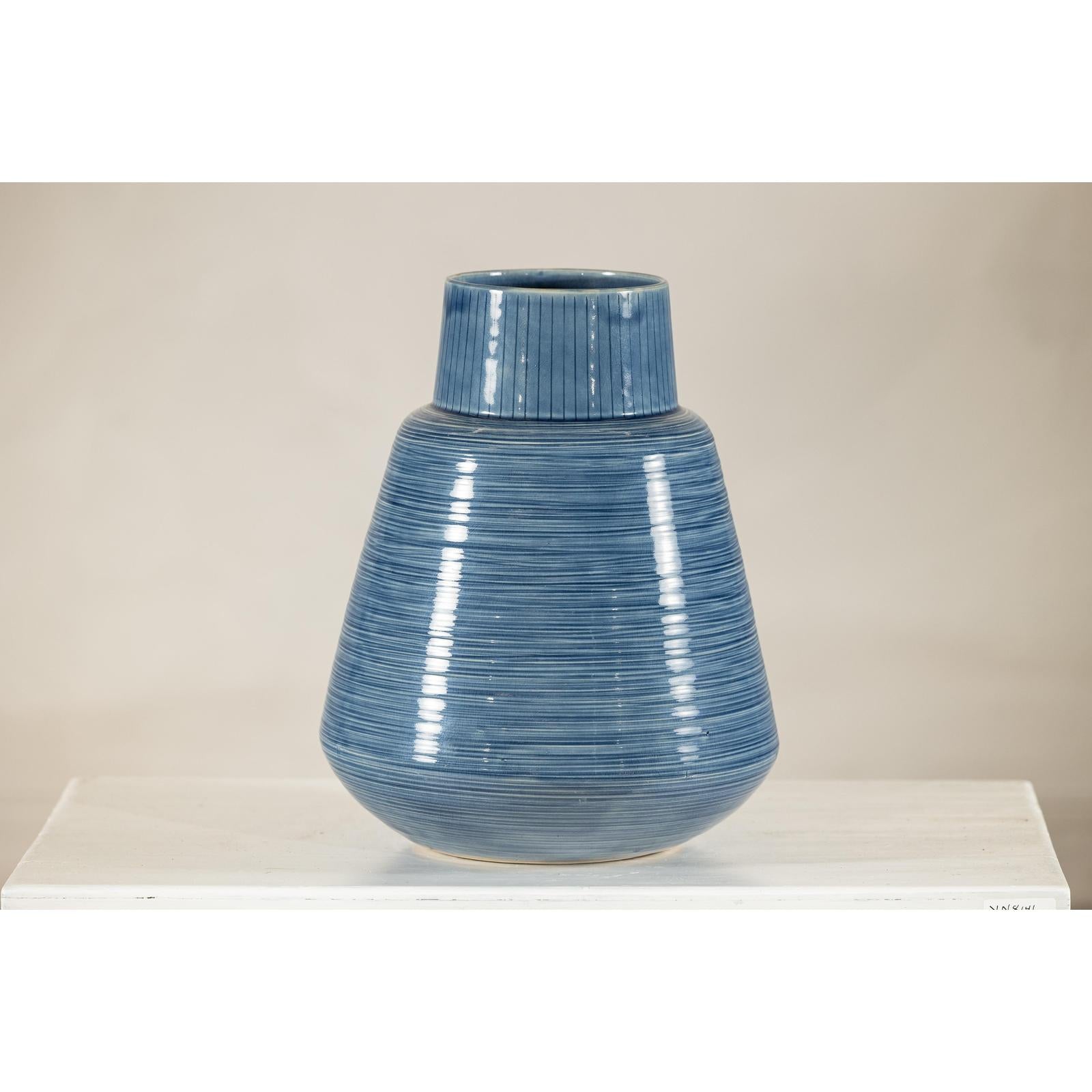 Blue-glazed ceramic vase with tapering form on a white surface, neutral background, close-up.