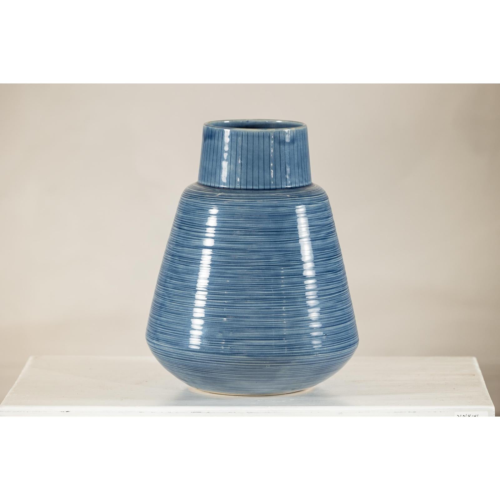 Close-up of a blue-glazed ceramic vase with tapering form on a white surface against a plain background.