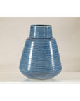 Close-up of a blue-glazed ceramic vase with tapering form on a white surface against a plain background.