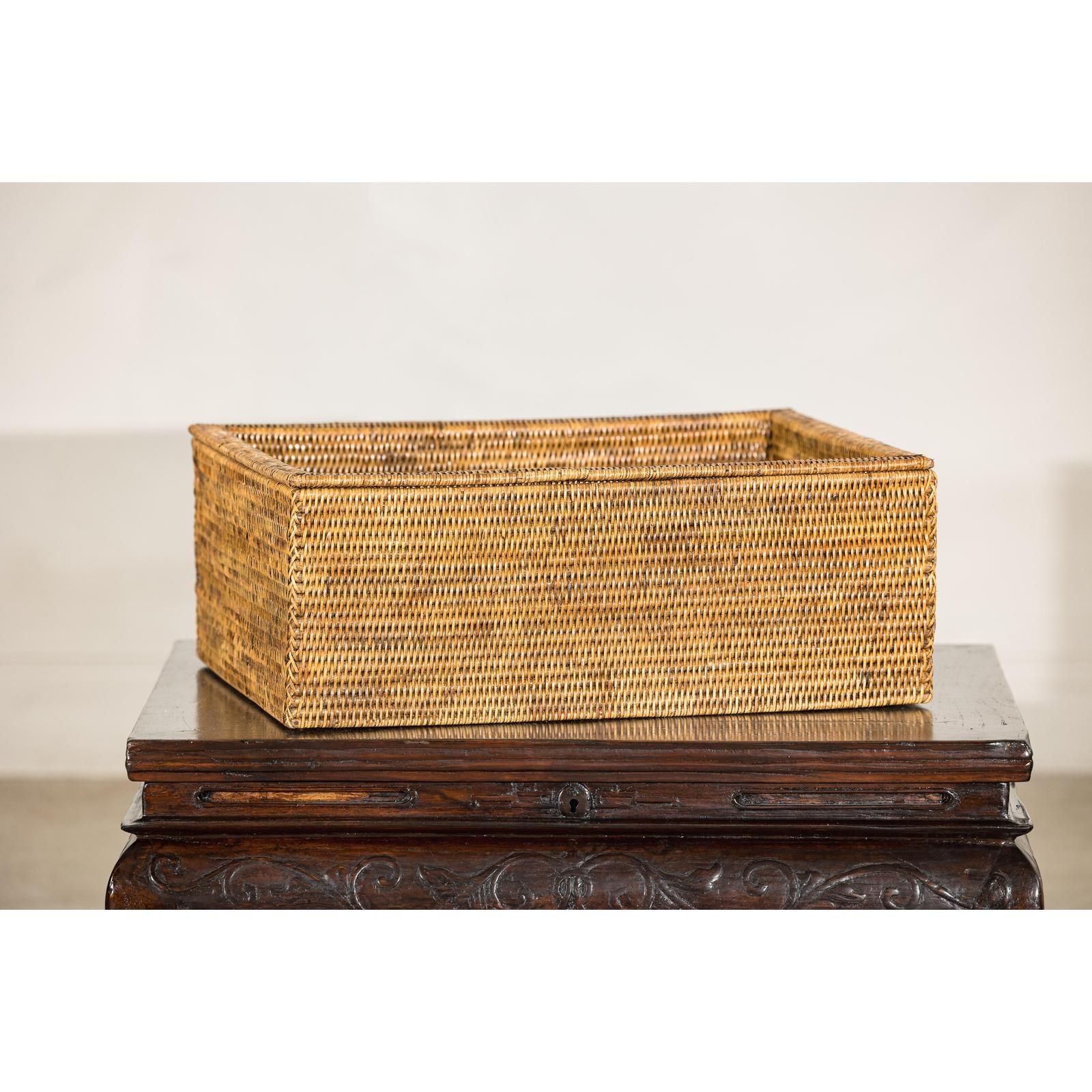 Long rectangular rattan storage box with lid, country style, on a carved dark wooden table.
