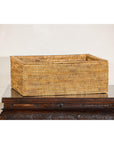 Long rectangular rattan storage box with lid, country style, on a carved dark wooden table.