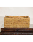 Brown rattan long rectangular storage box with lid on carved wooden table, plain background.