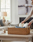 FEA Home vintage rectangular handwoven rattan basket with dark wood handles holding textiles on a living room table.