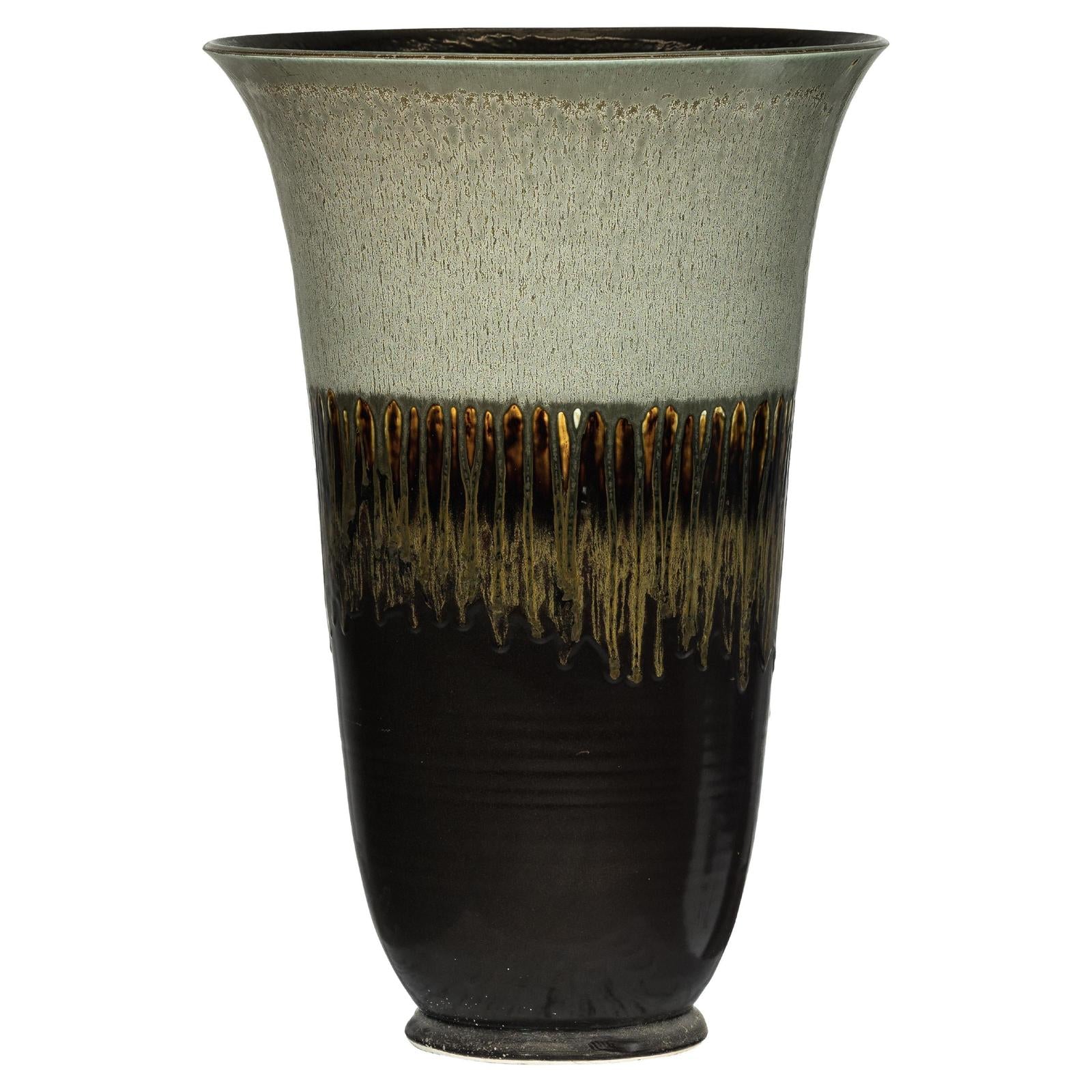 Close-up of a green-grey and brown ceramic planter with drip glaze, flared rim, and textured center pattern.