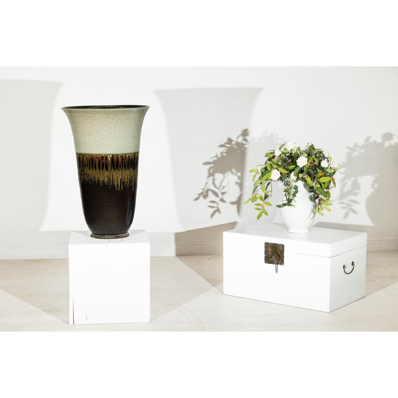 Green-grey and brown ceramic planter with drip glaze on white boxes against plain background, close-up.