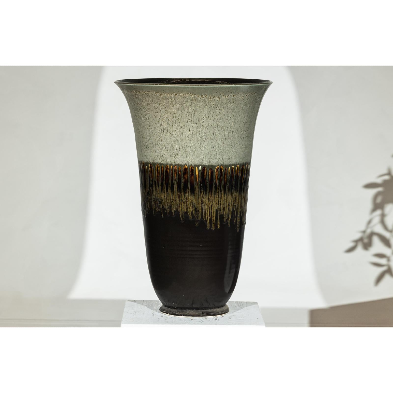 Close-up of a large handmade ceramic planter with green-grey to brown drip glaze and wide flared rim.
