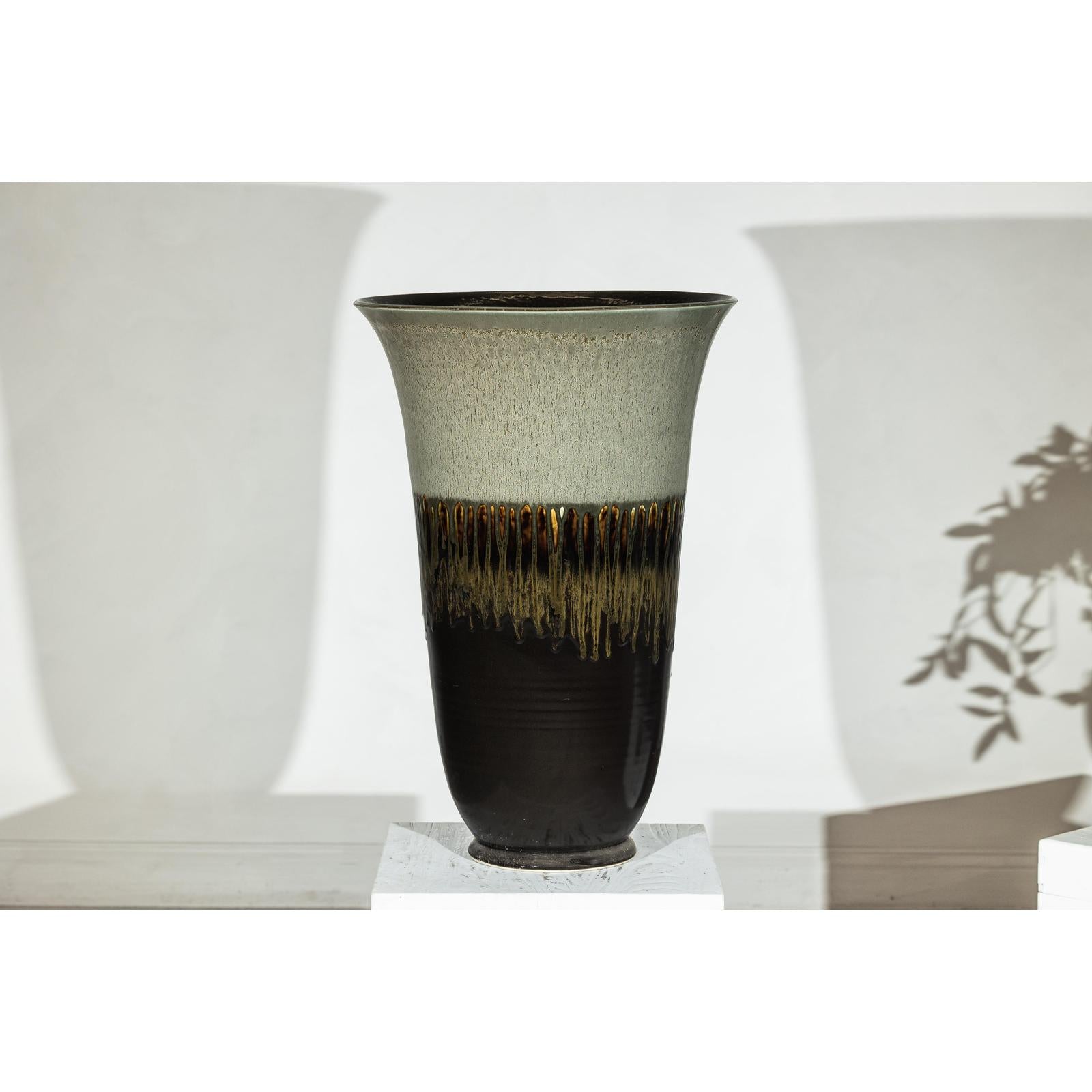 Green-grey and brown ceramic planter with drip glaze, flared rim, close-up on white pedestal.