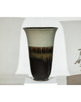 Green-grey and brown ceramic planter with drip glaze, flared rim, close-up on white pedestal.