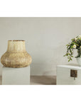 Cream and earth-toned textured ceramic vase on pedestal next to white chest with a flower vase in background.