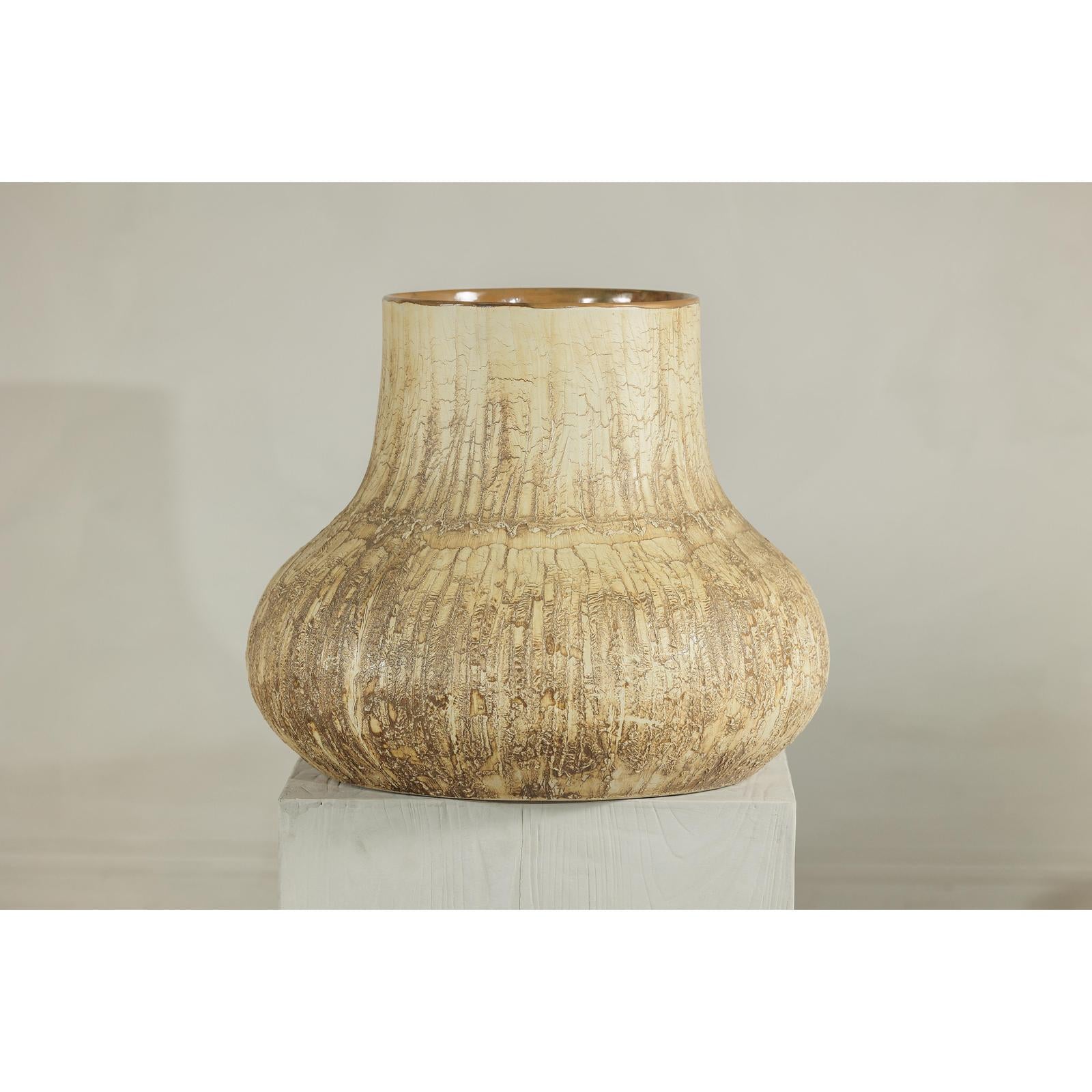 Textured cream and earth-toned ceramic vase on a white pedestal with a neutral background.