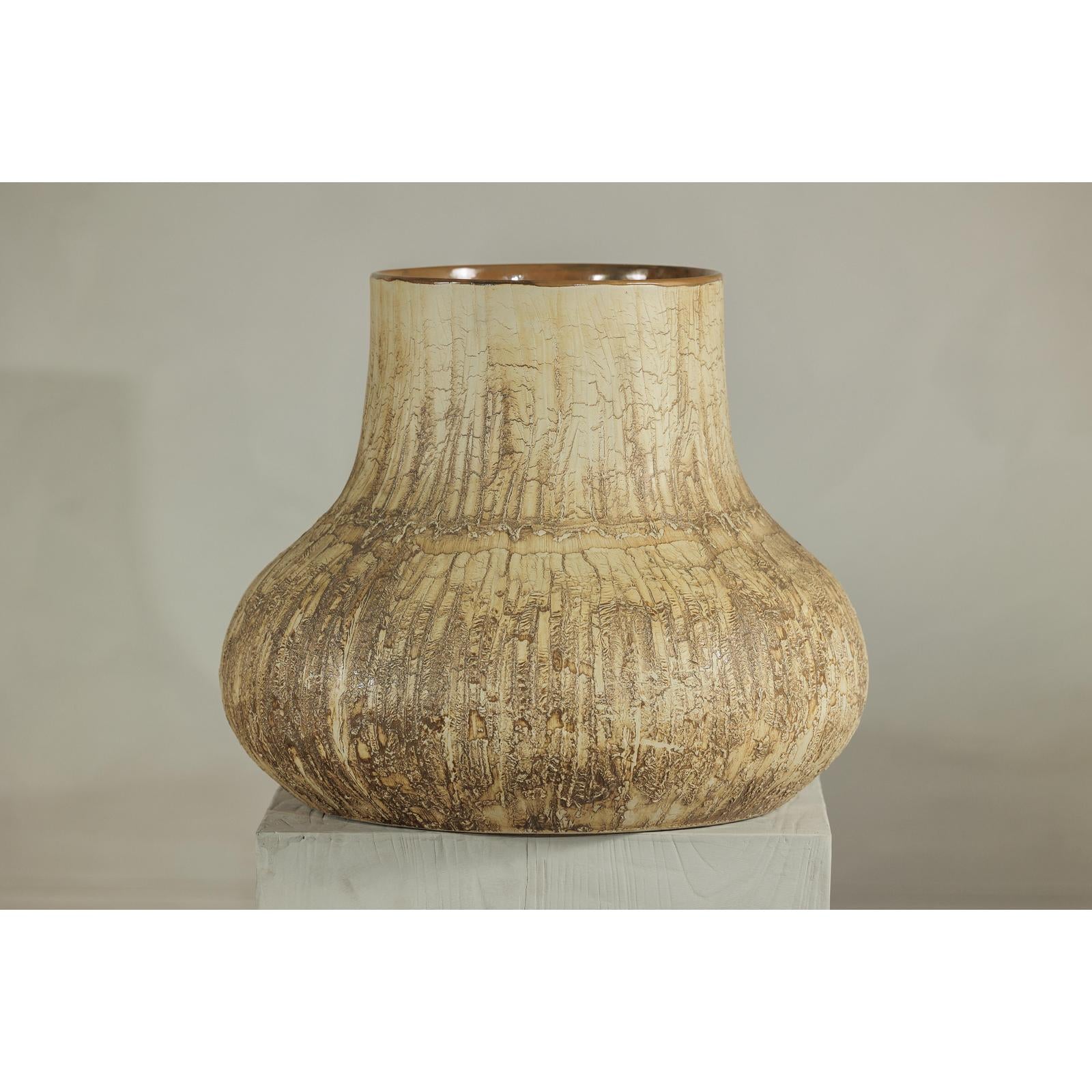 Cream and earth-toned textured ceramic vase on white pedestal, neutral background, close-up view.
