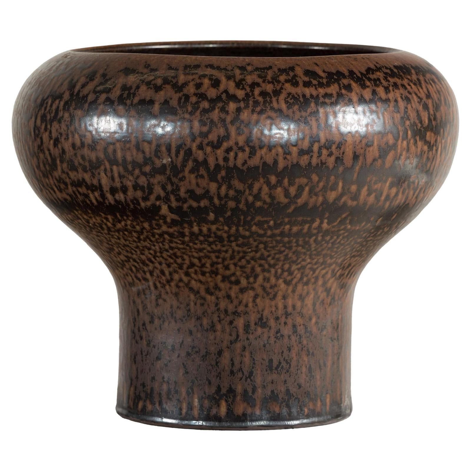 Close-up of a brown speckled ceramic vase with wide mouth, flared base, and textured artisan finish.