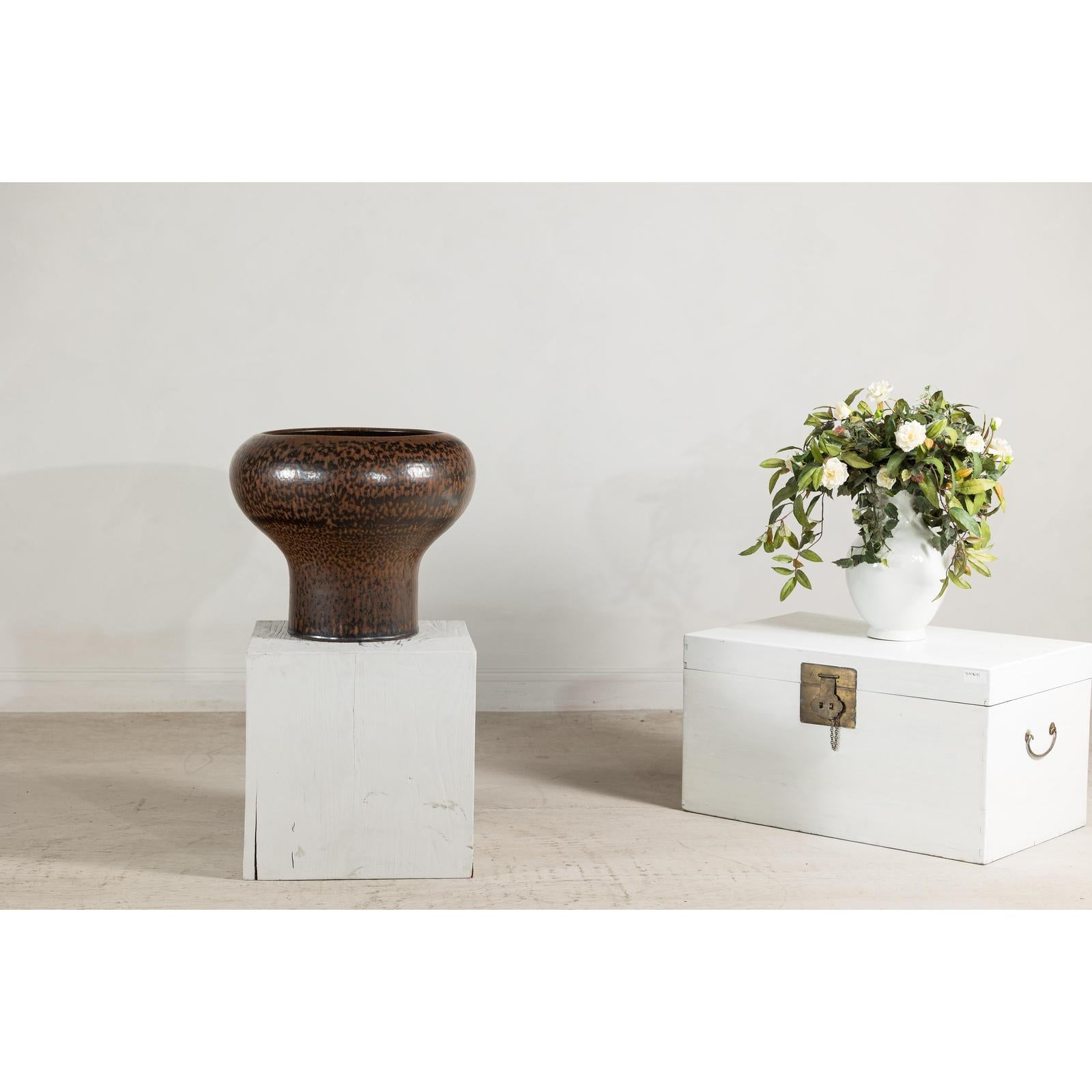 Dark studio pottery bowl and large speckled brown ceramic vase with wide mouth on white wooden boxes.