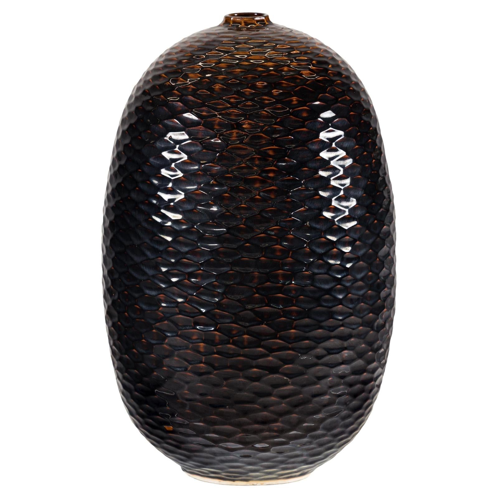 Close-up of deep brown and black ceramic vase with honeycomb texture, small opening, and sculptural oval shape.