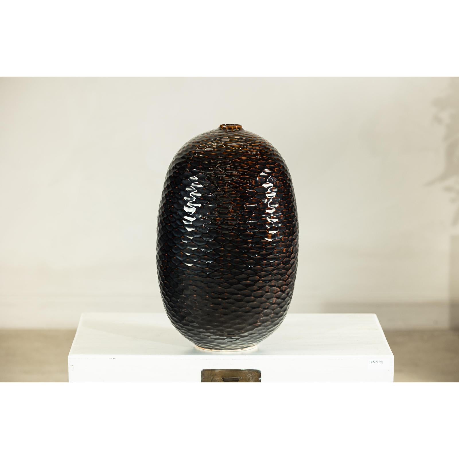 Deep brown and black ceramic vase with honeycomb texture on a white platform against a plain background.