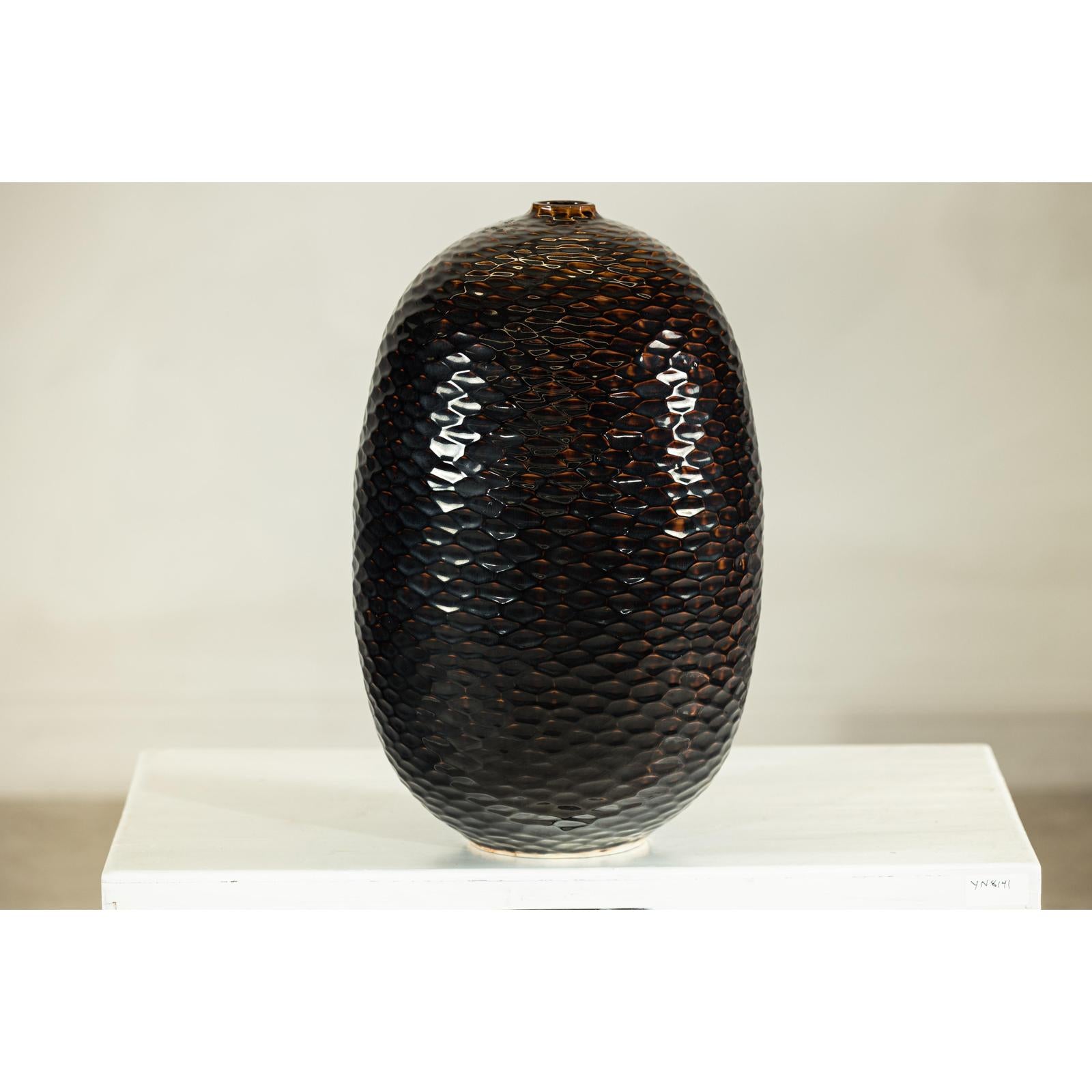 Deep brown and black ceramic vase with honeycomb-textured, scale-like surface against a white background.