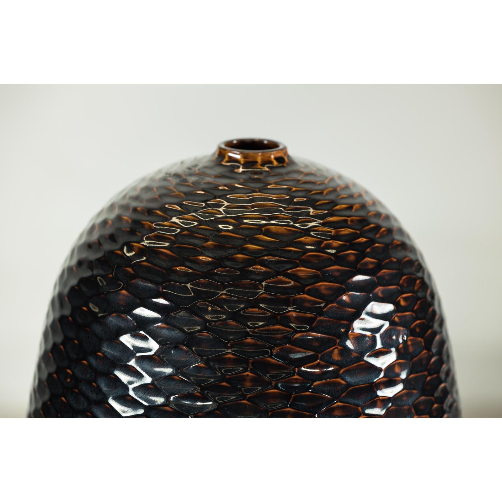 Close-up of a deep brown and black ceramic vase with honeycomb texture and small top opening.