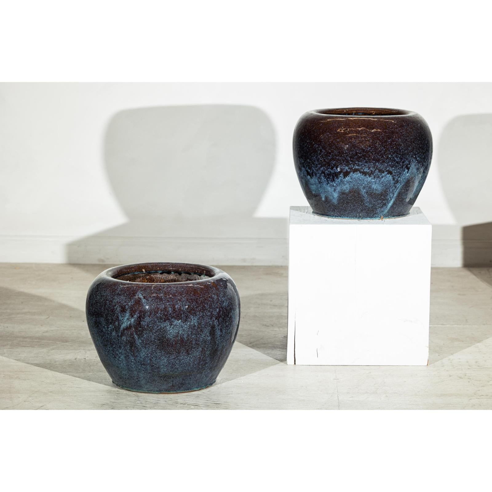 Close-up of two vintage blue and aqua glazed ceramic planters; one on the floor, one on a white pedestal.