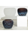 Close-up of two vintage blue and aqua glazed ceramic planters; one on the floor, one on a white pedestal.