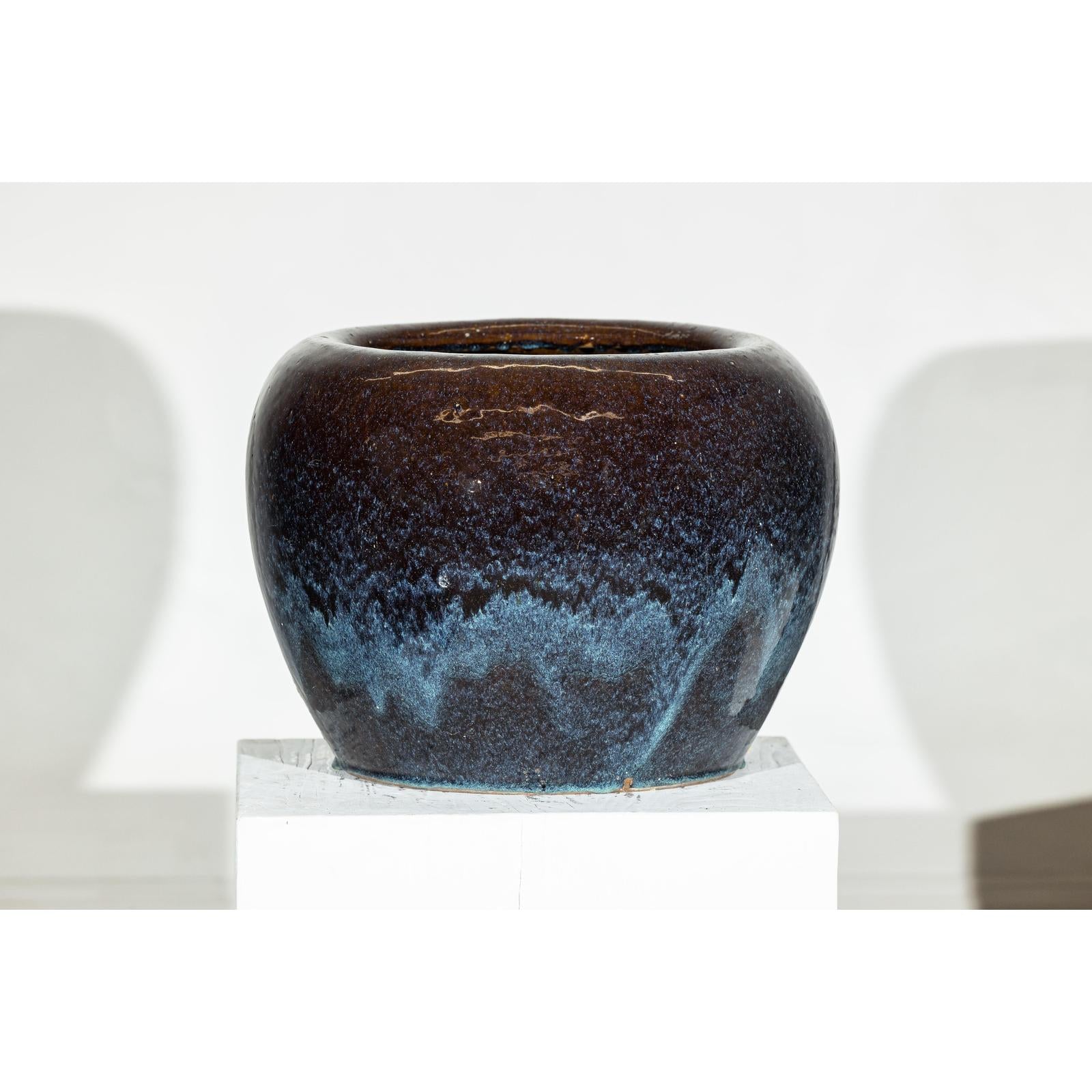 Close-up of two vintage blue and aqua glazed ceramic planters on a white pedestal against a white background.