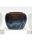 Close-up of two vintage blue and aqua glazed ceramic planters on a white pedestal against a white background.