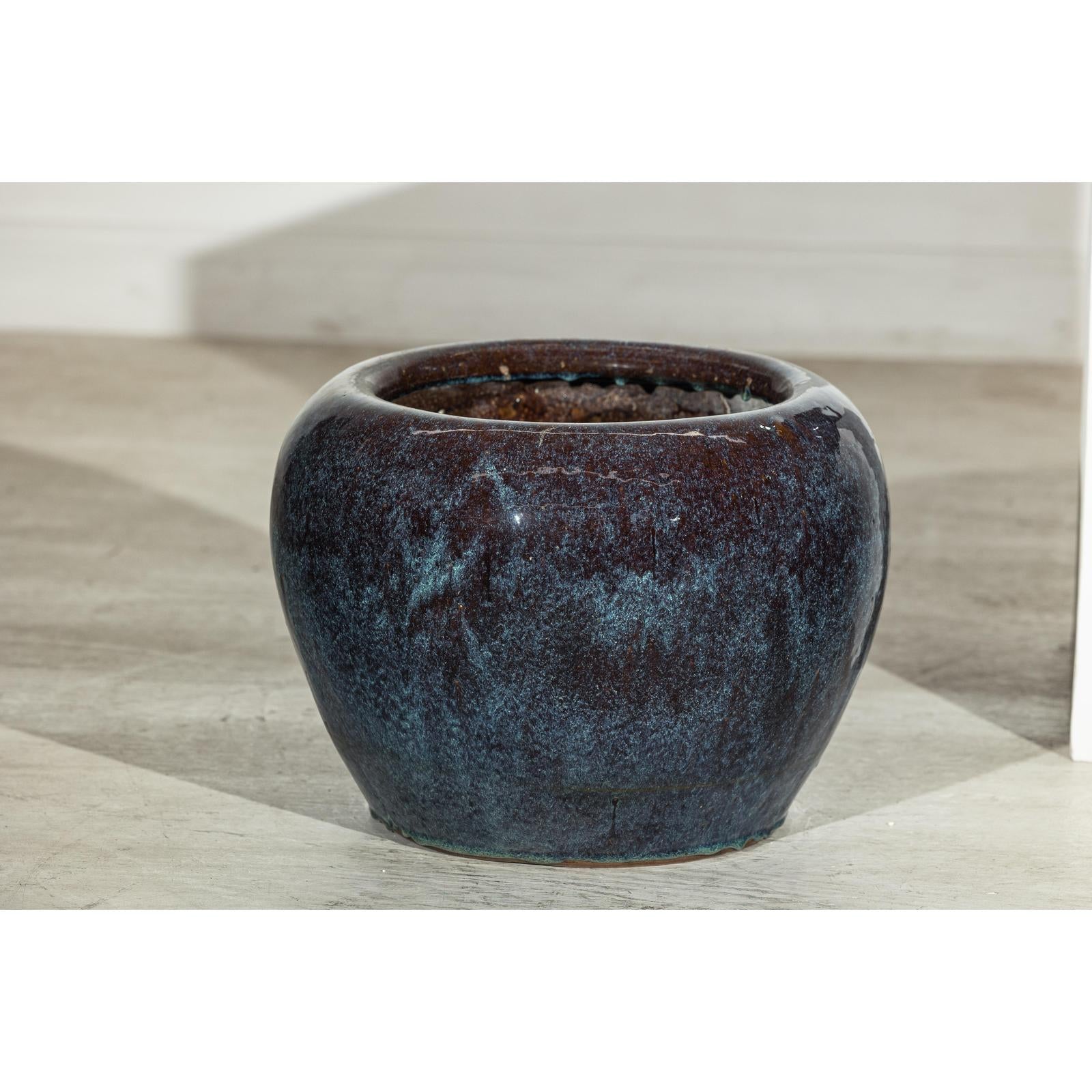 Close-up of vintage blue and aqua glazed ceramic planters on a light floor against a white wall.
