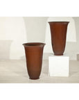 Brown ceramic vases with red undertones, one on the floor and one on a white pedestal against a light wall.