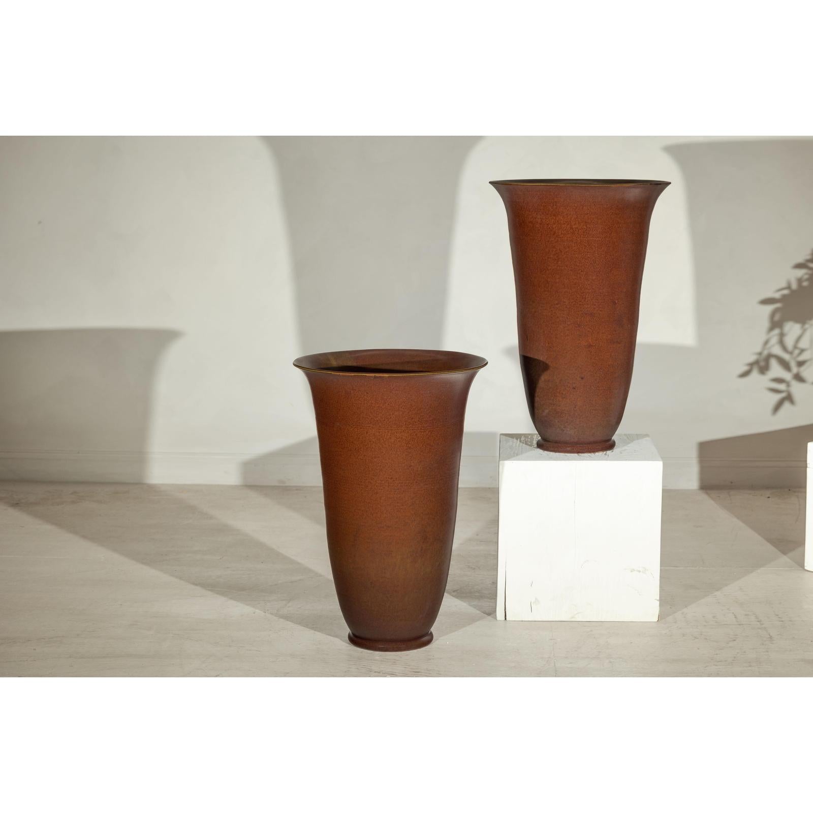 Brown ceramic vases with subtle red undertones on a light floor next to a white pedestal.