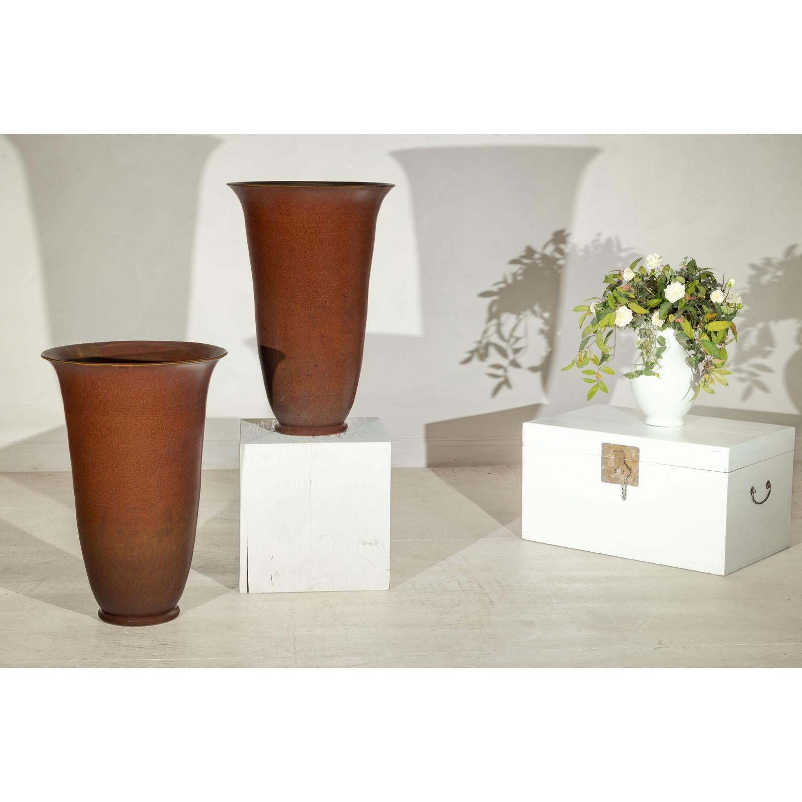 Brown ceramic vases with red undertones on white stands next to a chest topped with a white vase, interior setting.