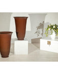 Brown ceramic vases with red undertones on white stands next to a chest topped with a white vase, interior setting.