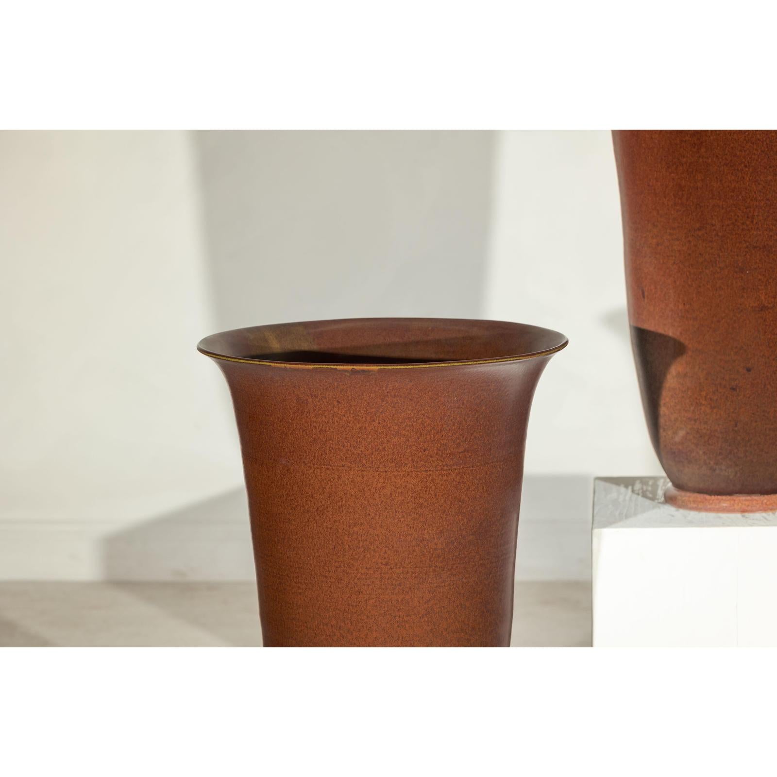 Brown ceramic vases with red undertones next to a white pedestal, close-up.